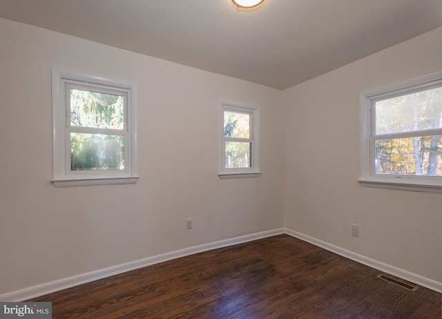 empty room featuring dark wood-style flooring, plenty of natural light, visible vents, and baseboards