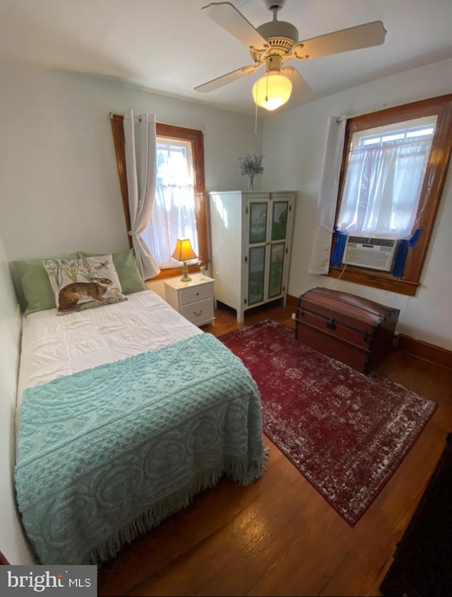 bedroom featuring a ceiling fan, cooling unit, baseboards, and wood finished floors