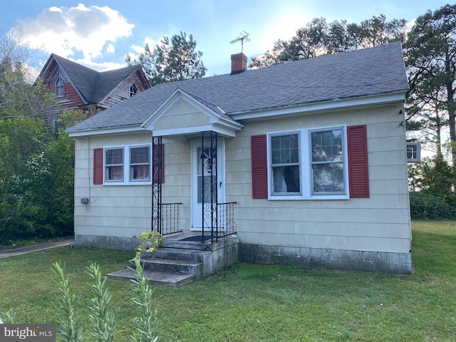 bungalow with a shingled roof, a chimney, and a front yard