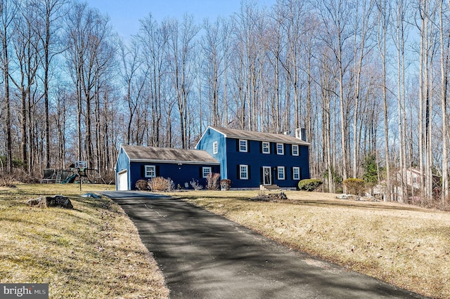 view of front of property featuring aphalt driveway, a front yard, an attached garage, and a chimney