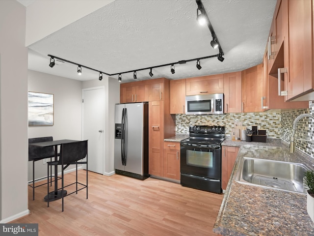 kitchen with tasteful backsplash, appliances with stainless steel finishes, a textured ceiling, light wood-style floors, and a sink