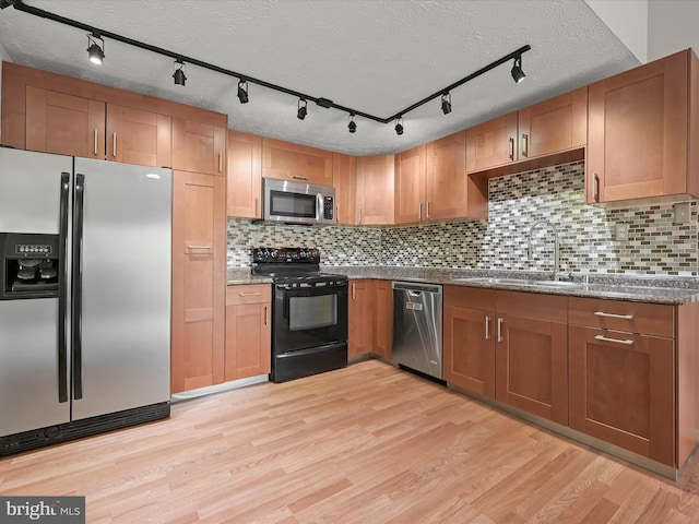 kitchen with appliances with stainless steel finishes, a sink, light wood-style flooring, and a textured ceiling