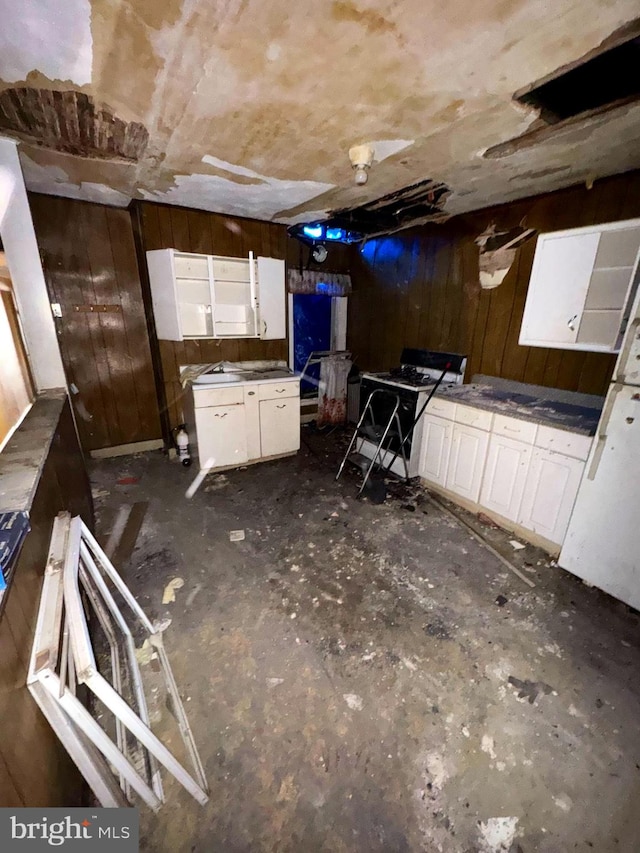 kitchen with white gas range oven, wooden walls, dark countertops, and white cabinets