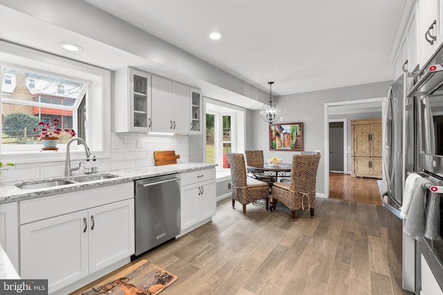 kitchen featuring white cabinets, decorative backsplash, glass insert cabinets, stainless steel dishwasher, and a sink