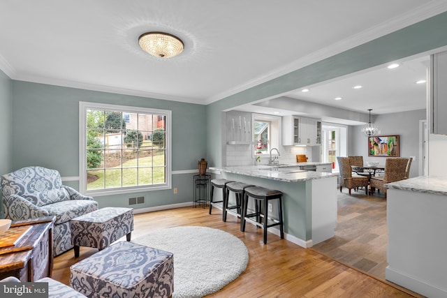 kitchen with light stone counters, a breakfast bar area, light wood finished floors, visible vents, and a peninsula