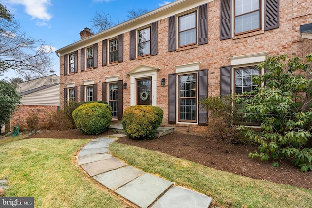 colonial inspired home with brick siding and a chimney