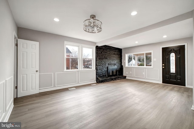 unfurnished living room with a fireplace, a decorative wall, a wealth of natural light, and wood finished floors