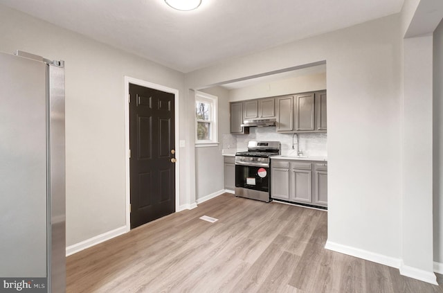 kitchen featuring decorative backsplash, gray cabinetry, stainless steel gas range, light wood-type flooring, and under cabinet range hood