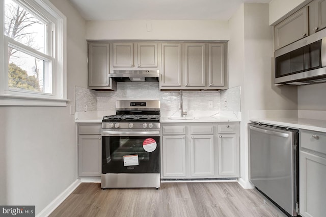 kitchen featuring under cabinet range hood, appliances with stainless steel finishes, gray cabinets, and light countertops