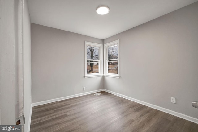 empty room with visible vents, dark wood finished floors, and baseboards