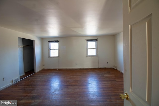 unfurnished bedroom featuring a closet, visible vents, multiple windows, and wood finished floors