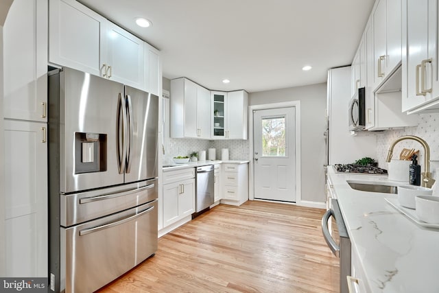 kitchen with white cabinets, appliances with stainless steel finishes, light stone countertops, light wood-type flooring, and a sink