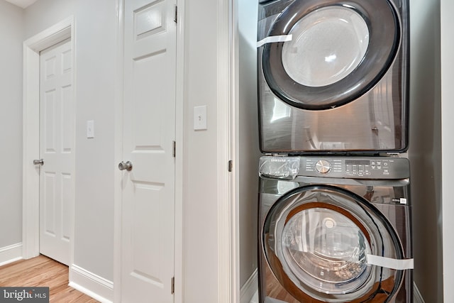 washroom with laundry area, baseboards, stacked washing maching and dryer, and wood finished floors