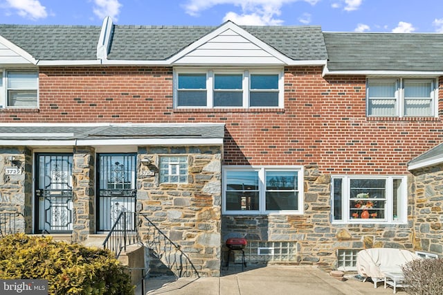 exterior space featuring stone siding, a patio area, brick siding, and roof with shingles