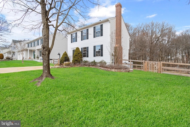 colonial home with a chimney, fence, and a front lawn