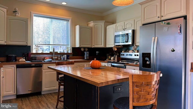 kitchen featuring crown molding, stainless steel appliances, a sink, a kitchen island, and butcher block countertops