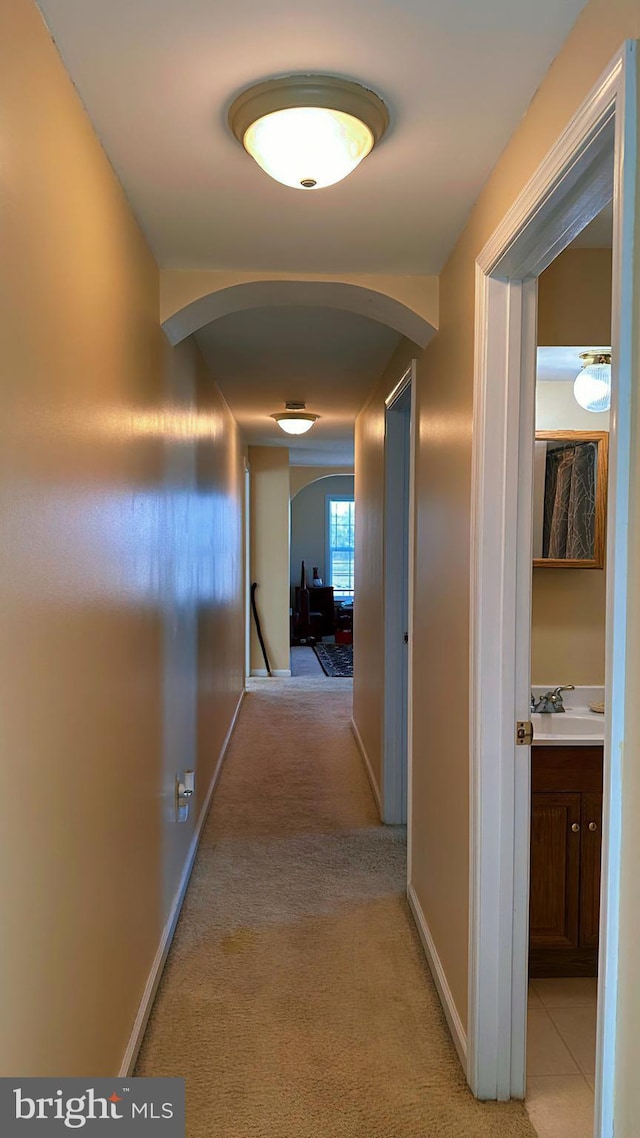 hallway with light carpet, a sink, arched walkways, and baseboards