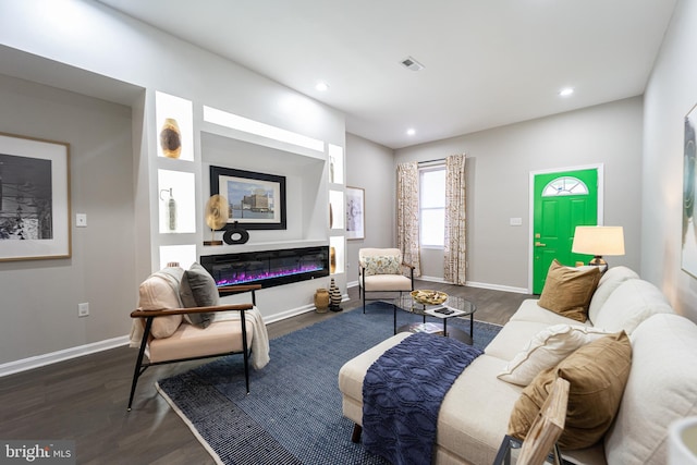 living area featuring baseboards, visible vents, dark wood-type flooring, and a glass covered fireplace