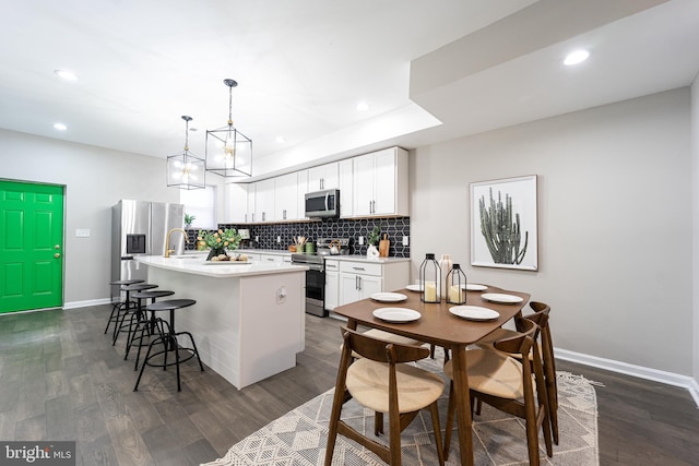 kitchen featuring a kitchen island with sink, stainless steel appliances, white cabinets, light countertops, and pendant lighting