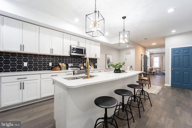 kitchen featuring an island with sink, stainless steel appliances, white cabinetry, pendant lighting, and a sink