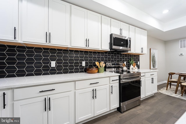 kitchen with dark wood-style floors, appliances with stainless steel finishes, white cabinets, and decorative backsplash