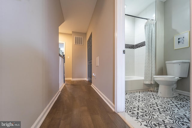 hallway with dark wood-type flooring, visible vents, and baseboards