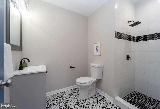 full bath with toilet, vanity, baseboards, tiled shower, and tile patterned floors