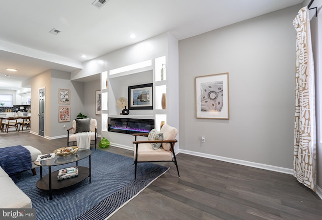 living room with recessed lighting, a glass covered fireplace, visible vents, baseboards, and dark wood finished floors