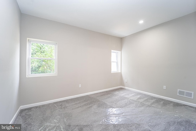 empty room featuring carpet floors, a healthy amount of sunlight, visible vents, and baseboards