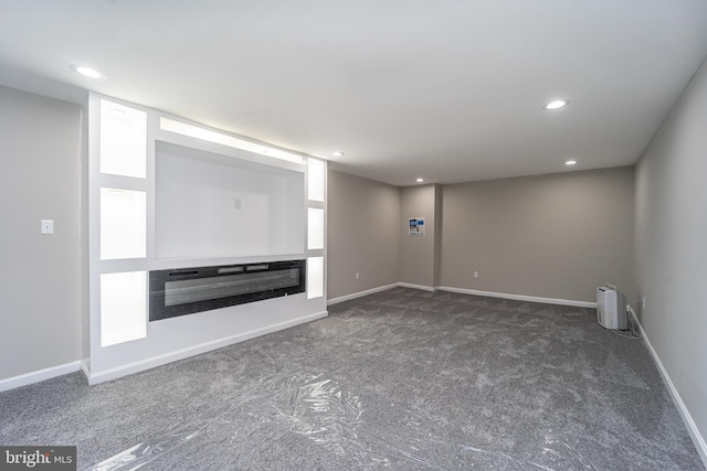 unfurnished living room with baseboards, dark carpet, a glass covered fireplace, and recessed lighting