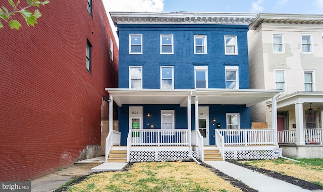 townhome / multi-family property with a porch and brick siding