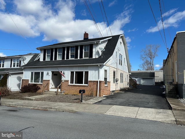 view of front of house featuring an outbuilding, driveway, a shingled roof, a chimney, and brick siding