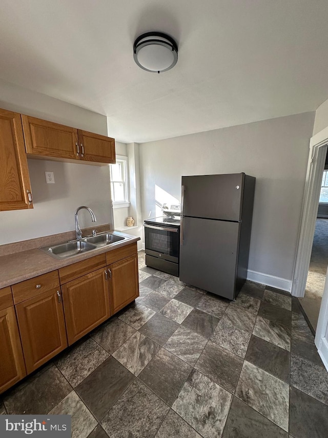 kitchen featuring baseboards, brown cabinets, stone finish floor, stainless steel appliances, and a sink