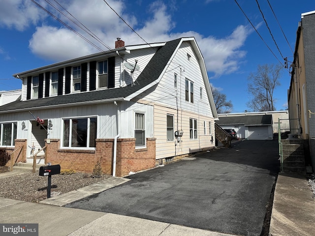 view of front of house featuring brick siding, an outbuilding, roof with shingles, and a chimney