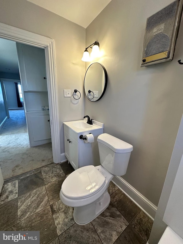 bathroom featuring vanity, toilet, baseboards, and stone finish flooring