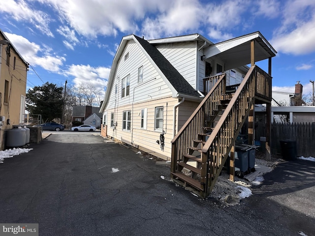 back of house with stairway, fence, aphalt driveway, and a shingled roof