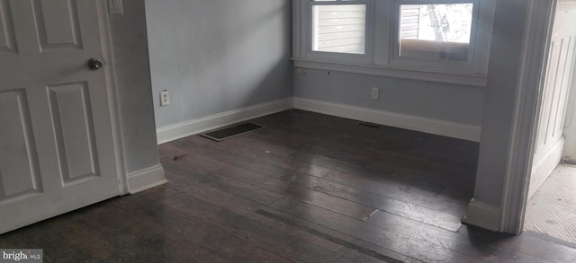 spare room with dark wood-style floors, visible vents, and baseboards