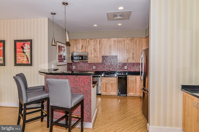 kitchen featuring dark countertops, stainless steel appliances, a breakfast bar, and light wood-type flooring