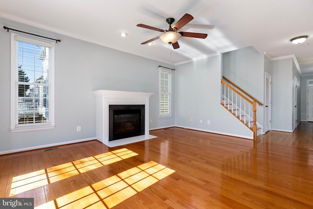 unfurnished living room featuring hardwood / wood-style flooring, a fireplace with flush hearth, baseboards, stairs, and ornamental molding