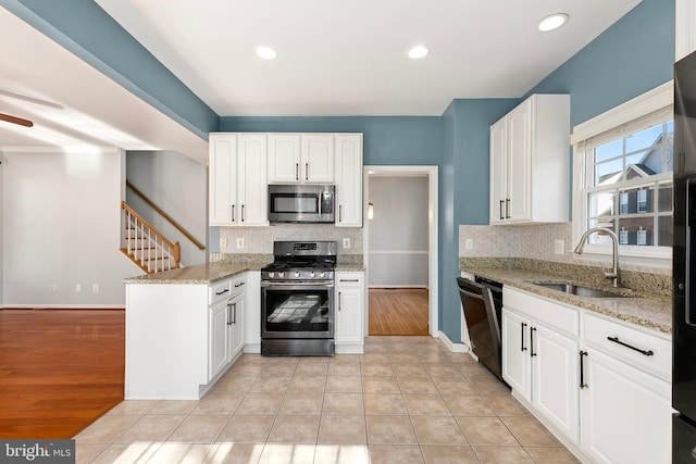 kitchen featuring stainless steel appliances, a peninsula, a sink, and light stone countertops