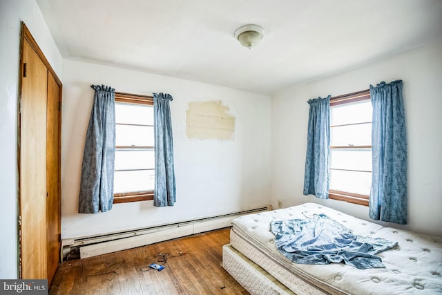 bedroom with a baseboard heating unit, multiple windows, and hardwood / wood-style floors