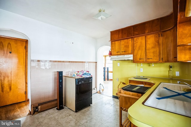 kitchen with arched walkways, under cabinet range hood, tile walls, light countertops, and brown cabinets