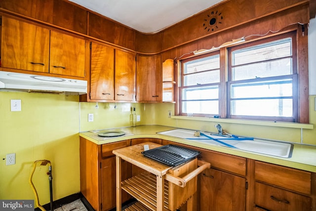 kitchen with brown cabinets, under cabinet range hood, light countertops, and a wealth of natural light