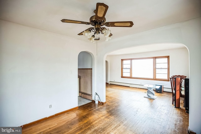 unfurnished room featuring baseboards, arched walkways, a ceiling fan, a baseboard radiator, and hardwood / wood-style floors