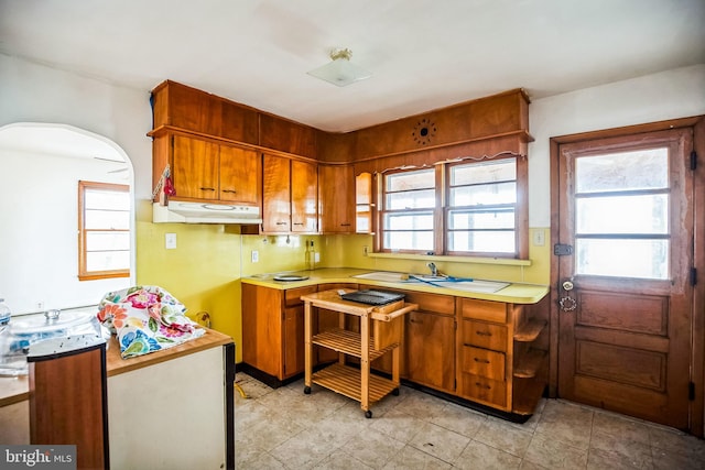 kitchen with light countertops, under cabinet range hood, a wealth of natural light, and brown cabinets