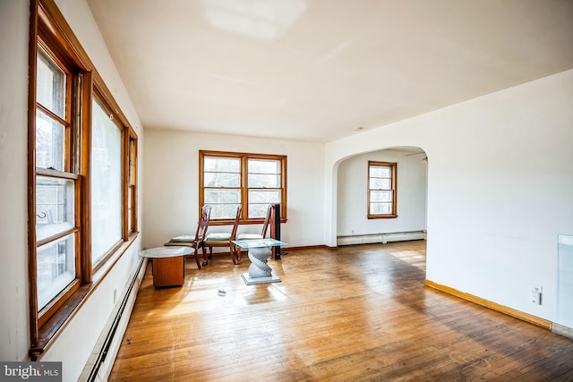 interior space featuring arched walkways, baseboard heating, and hardwood / wood-style flooring