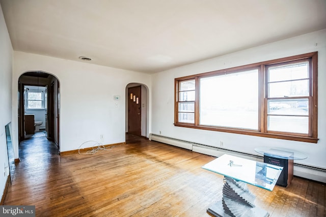 unfurnished living room with baseboards, visible vents, arched walkways, and hardwood / wood-style floors