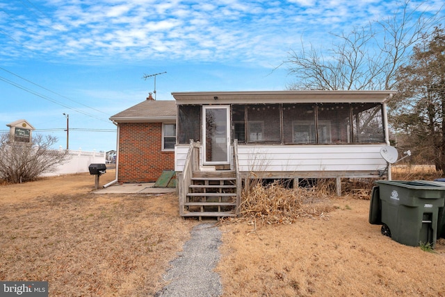 view of front of house featuring entry steps, brick siding, a front lawn, and a sunroom