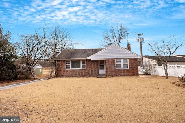 ranch-style home with brick siding, a front lawn, a chimney, and fence