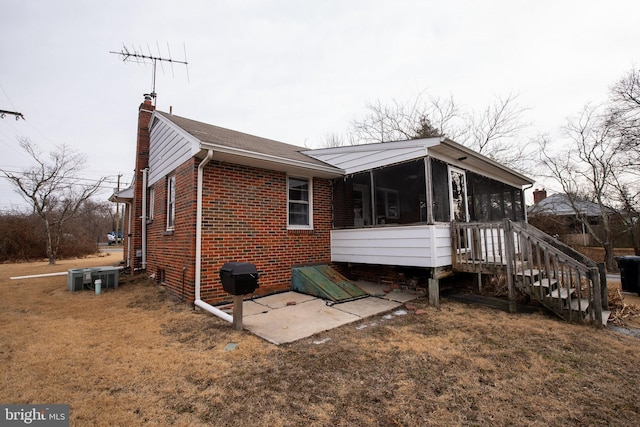 exterior space with brick siding, a chimney, a lawn, a sunroom, and a patio area